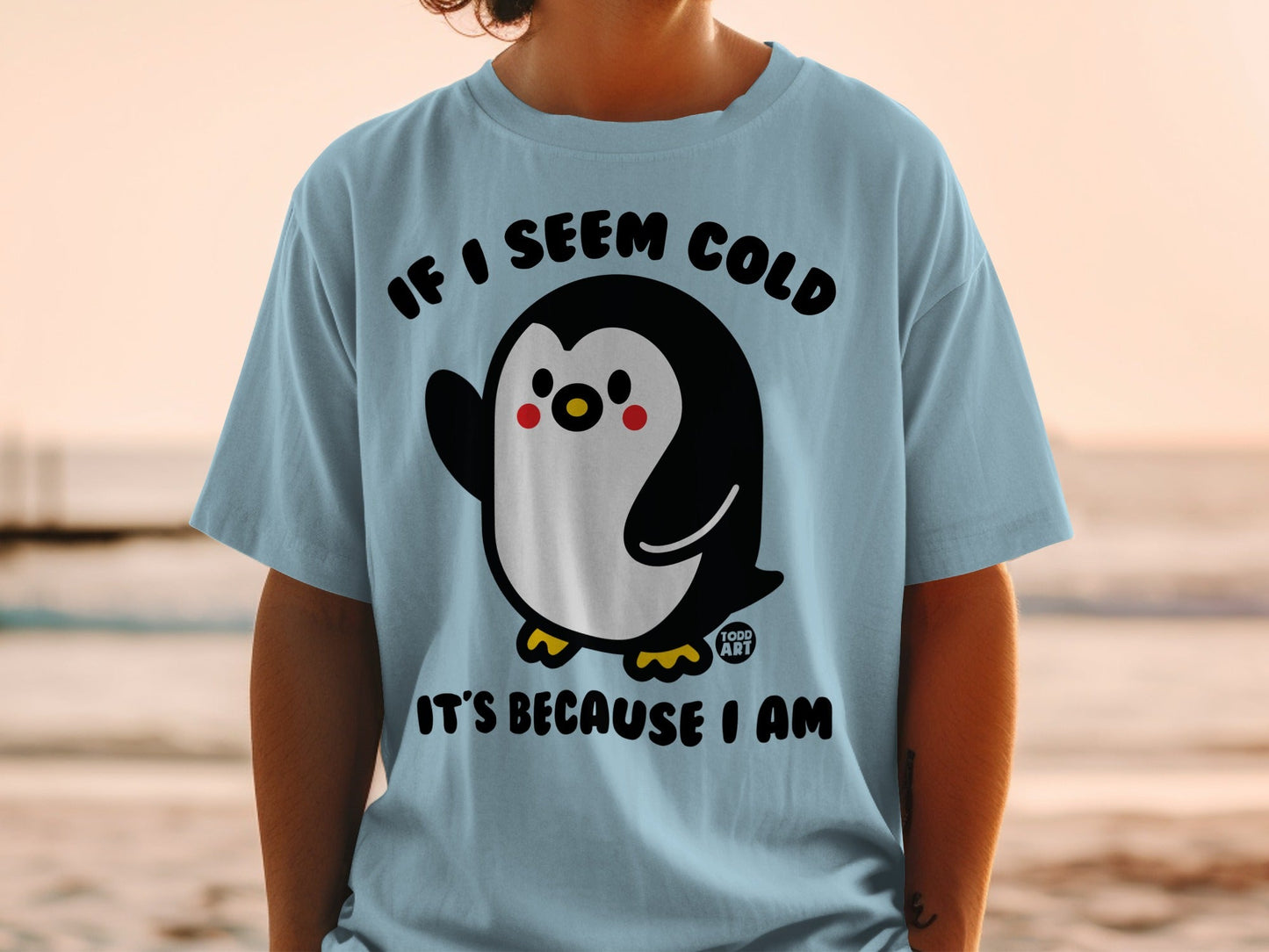 Light blue t-shirt with a cartoon penguin waving and text "IF I SEEM COLD IT'S BECAUSE I AM."