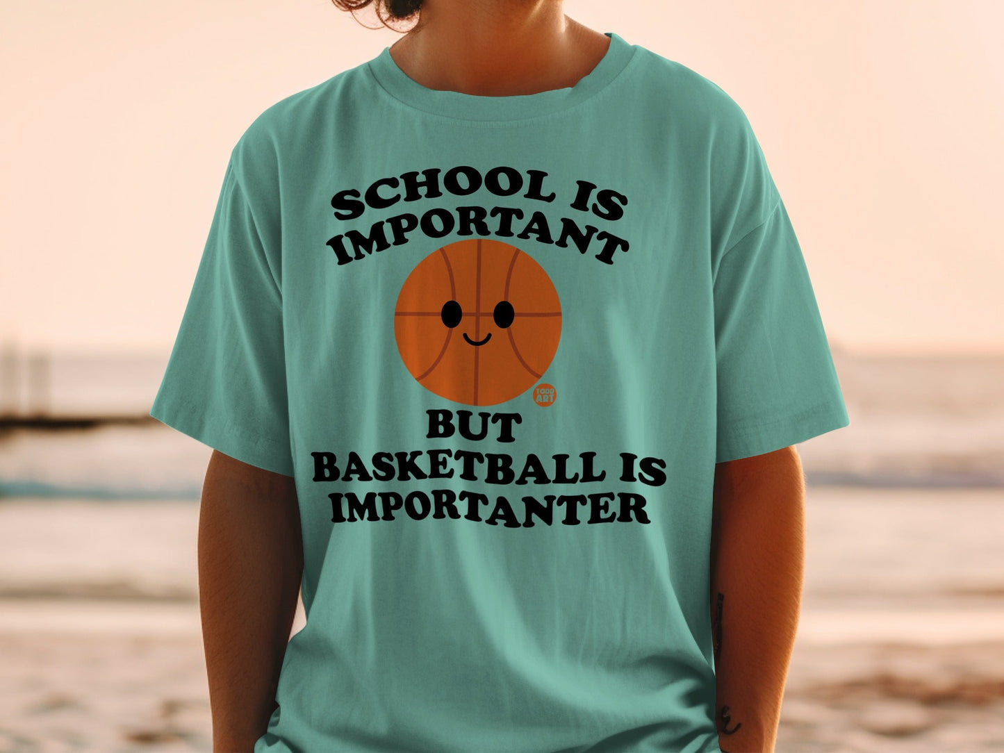 Teal t-shirt with text "SCHOOL IS IMPORTANT BUT BASKETBALL IS IMPORTANTER" and a smiling basketball.