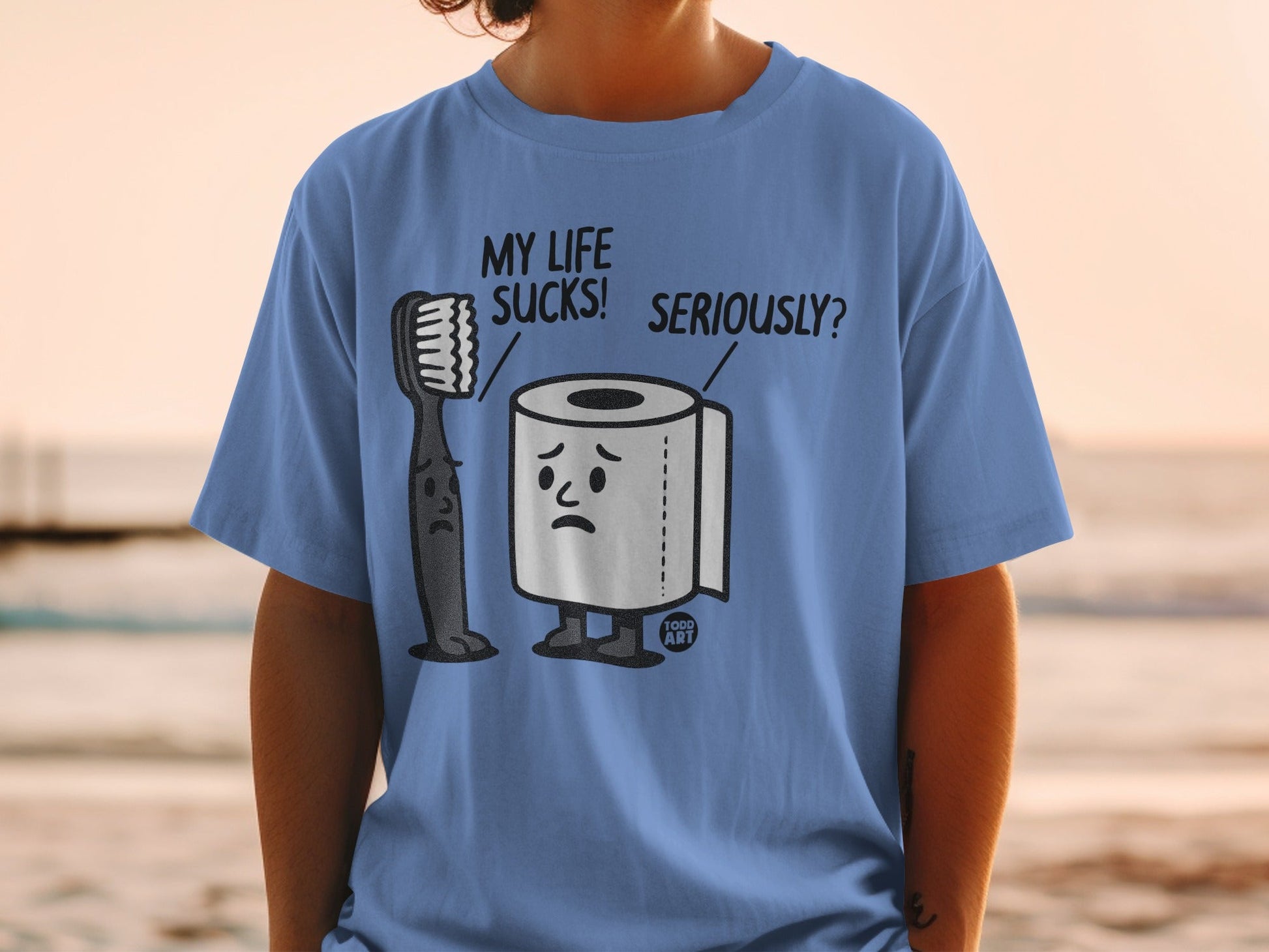 Blue t-shirt with sad toothbrush and toilet paper characters on it.