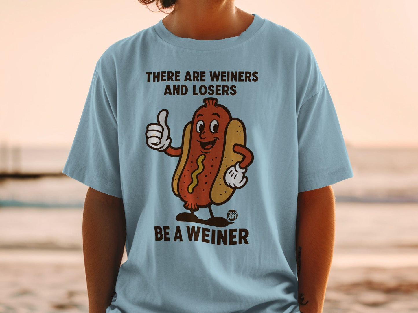 Light blue t-shirt with cartoon hot dog giving thumbs up and text "There are wieners and losers. Be a wiener."