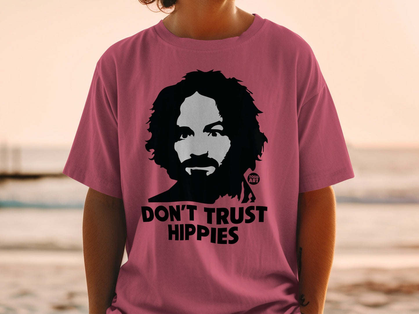 Pink t-shirt with a black graphic of a man's face and text "DON'T TRUST HIPPIES".