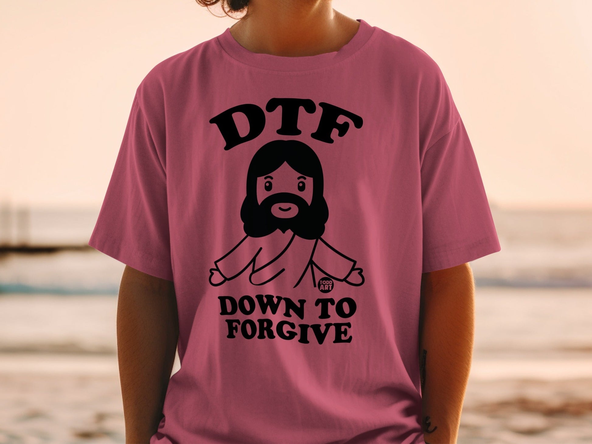Pink t-shirt with "DTF DOWN TO FORGIVE" text and cartoon Jesus graphic.
