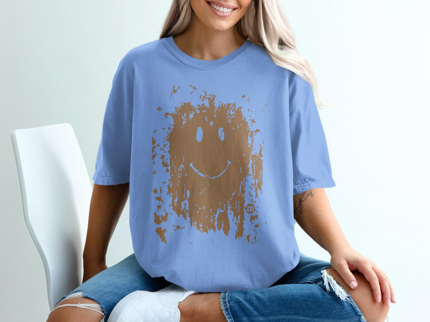 Blue t-shirt with distressed brown smiley face graphic, worn by a person.