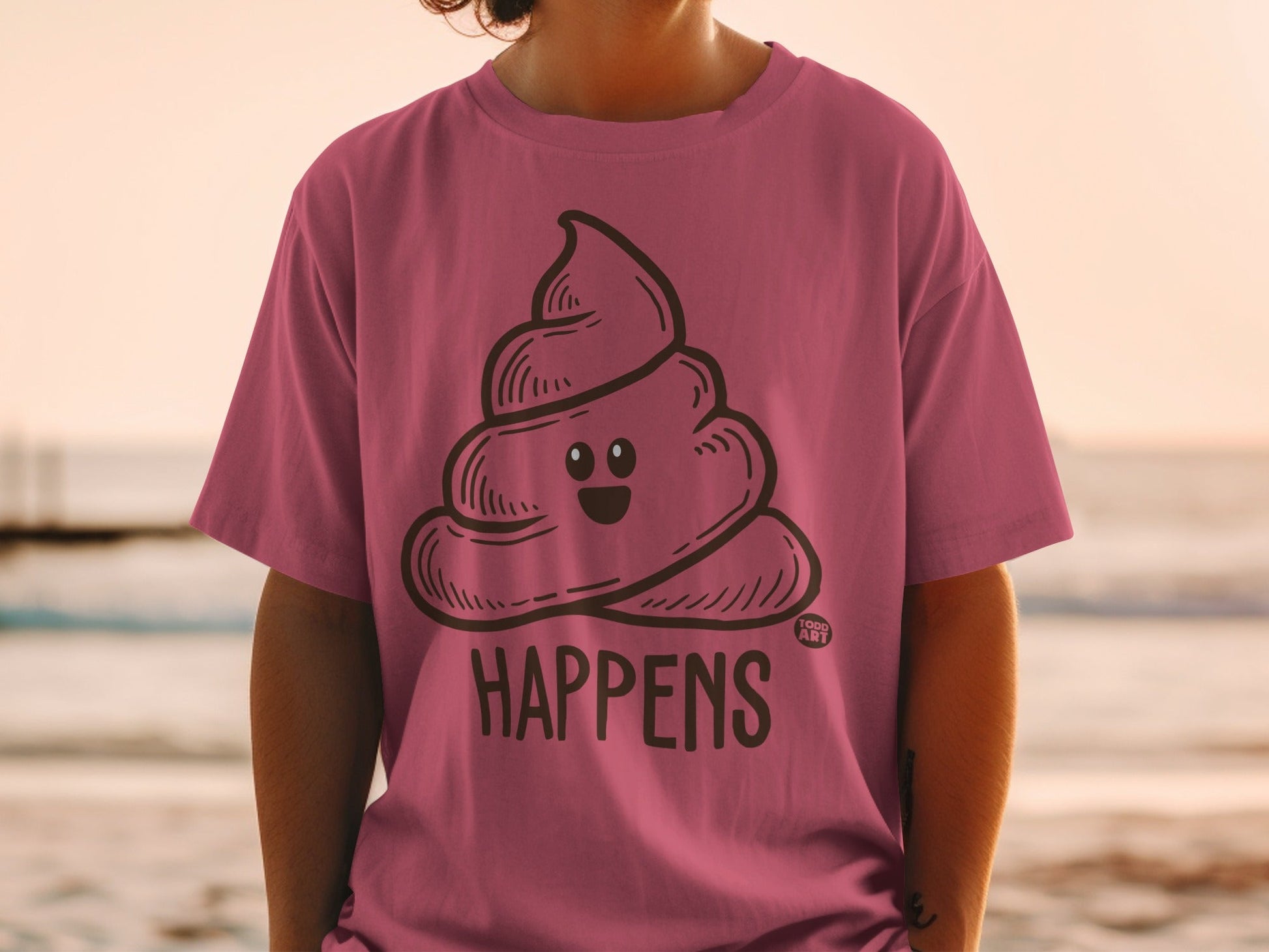 Pink t-shirt with a smiling pile of cartoon poop and the text "SHIT HAPPENS".