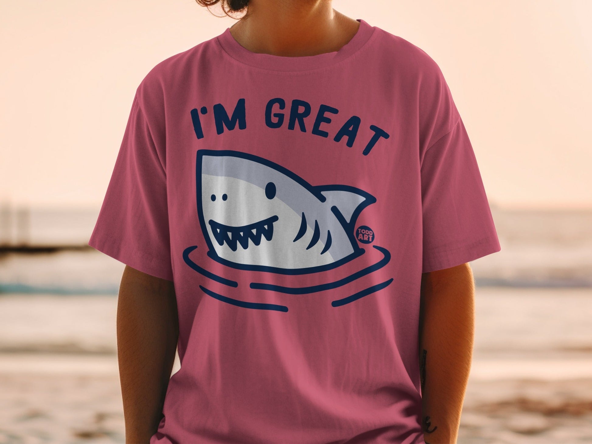Pink t-shirt with cartoon shark saying "I'm Great" at the beach.