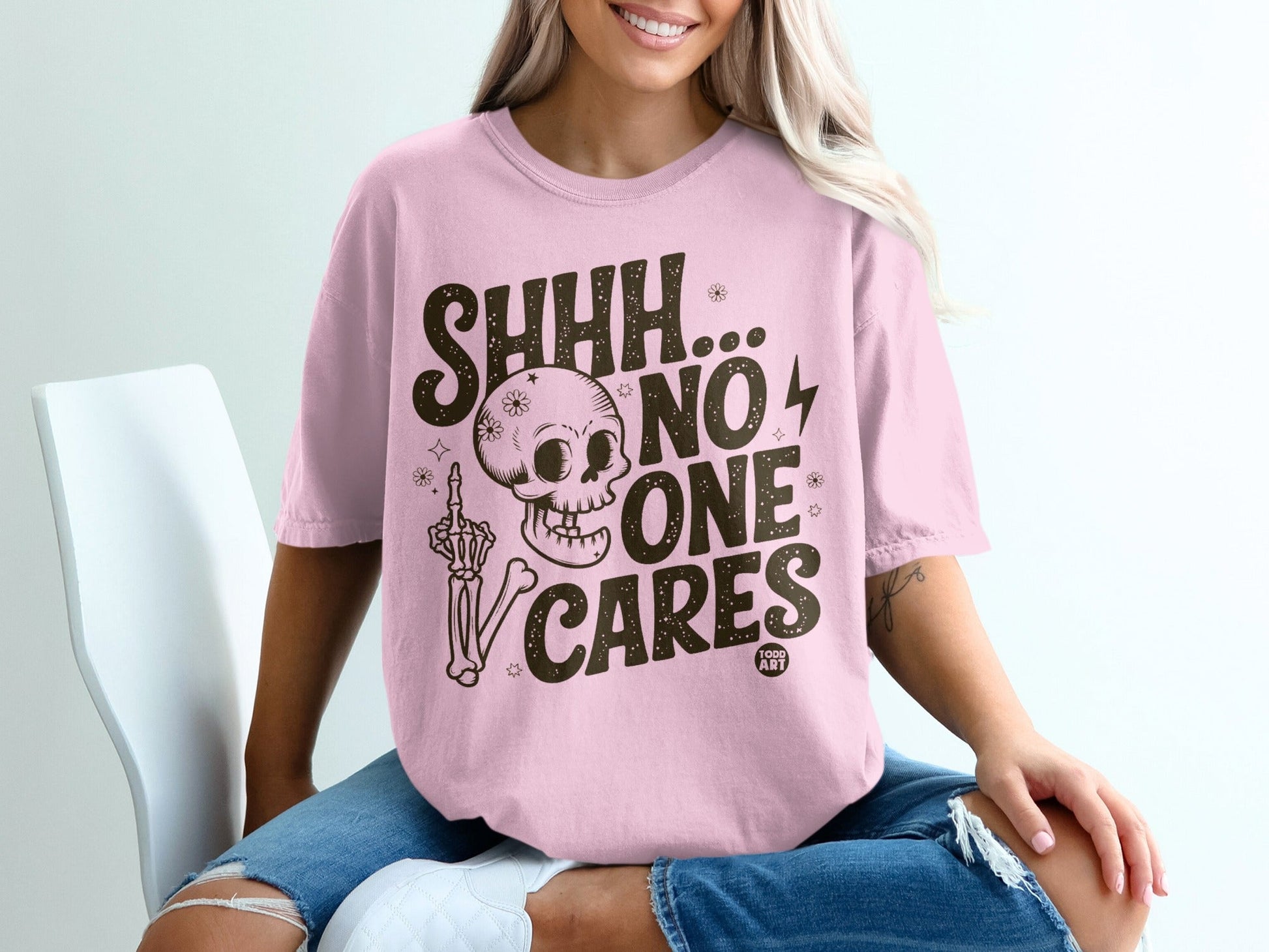 Pink t-shirt with skeleton, middle finger, and text "SHHH... NO ONE CARES".