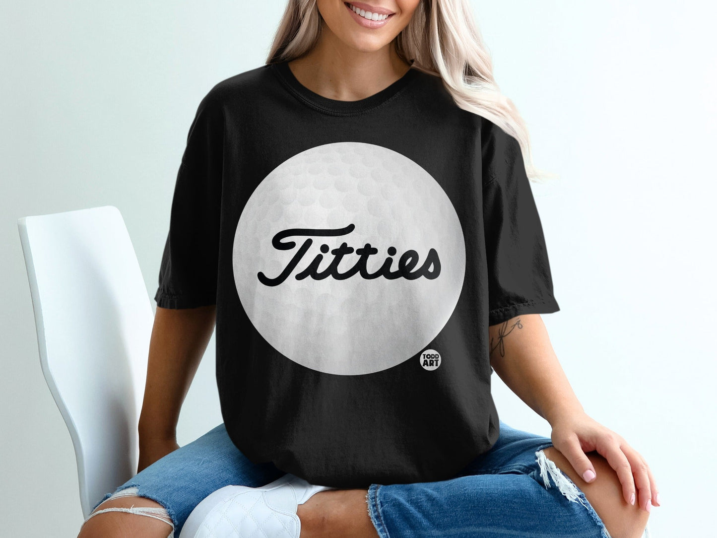 Black t-shirt with a large white golf ball and the word "Titties" in cursive.