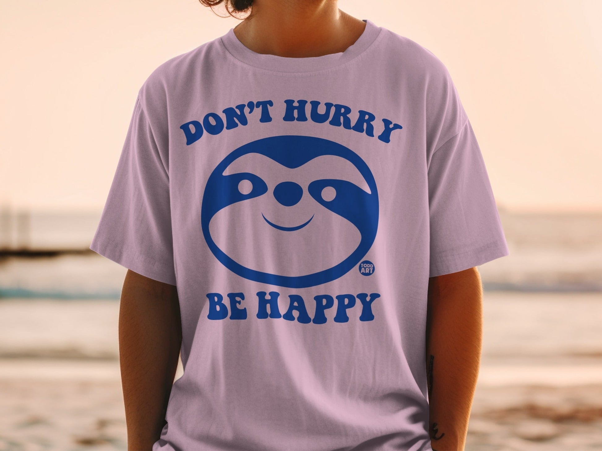 Purple t-shirt with blue sloth graphic and text "Don't Hurry Be Happy."
