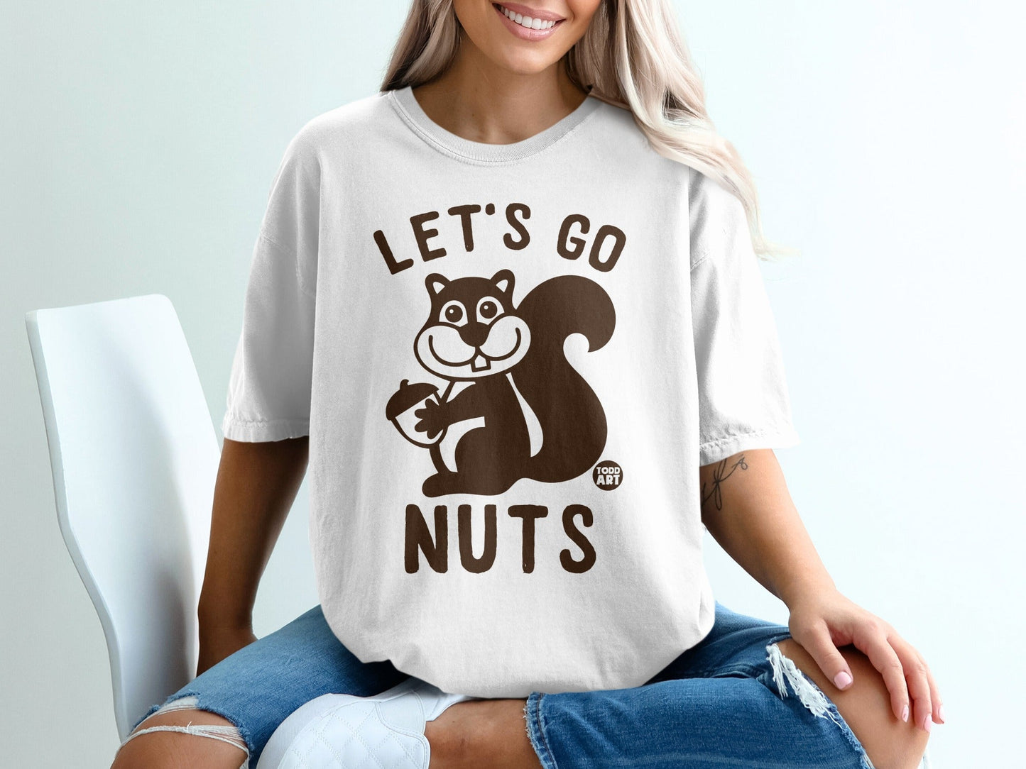 White t-shirt with cartoon squirrel holding acorn and text "LET'S GO NUTS".