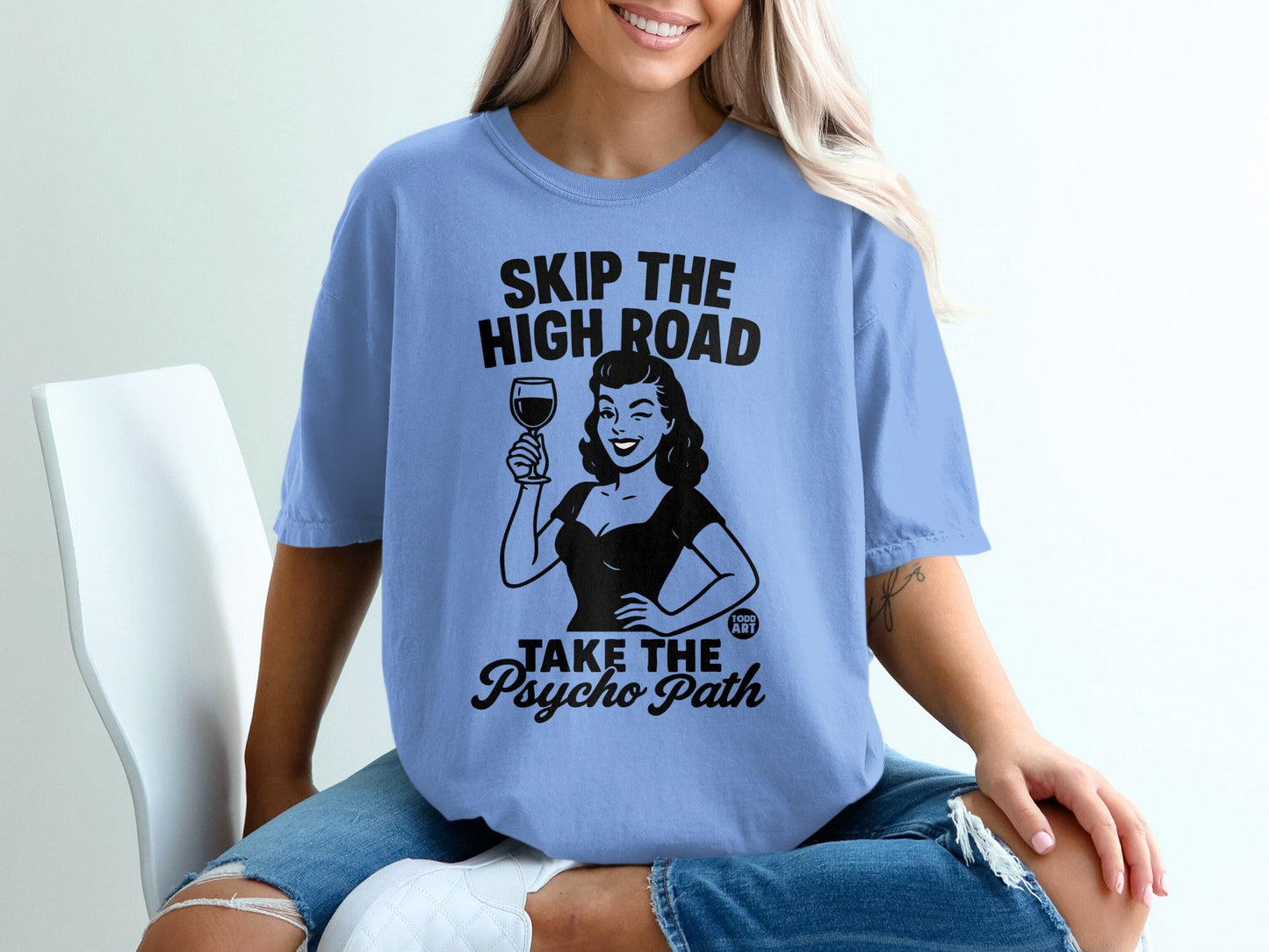 Light blue t-shirt with "SKIP THE HIGH ROAD TAKE THE PSYCHO PATH" text and retro woman illustration.
