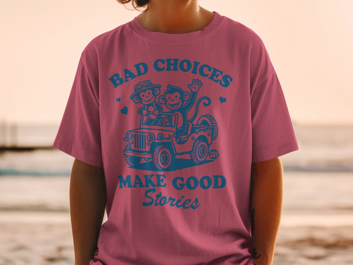 Pink t-shirt with blue graphic of two monkeys in a jeep and text.