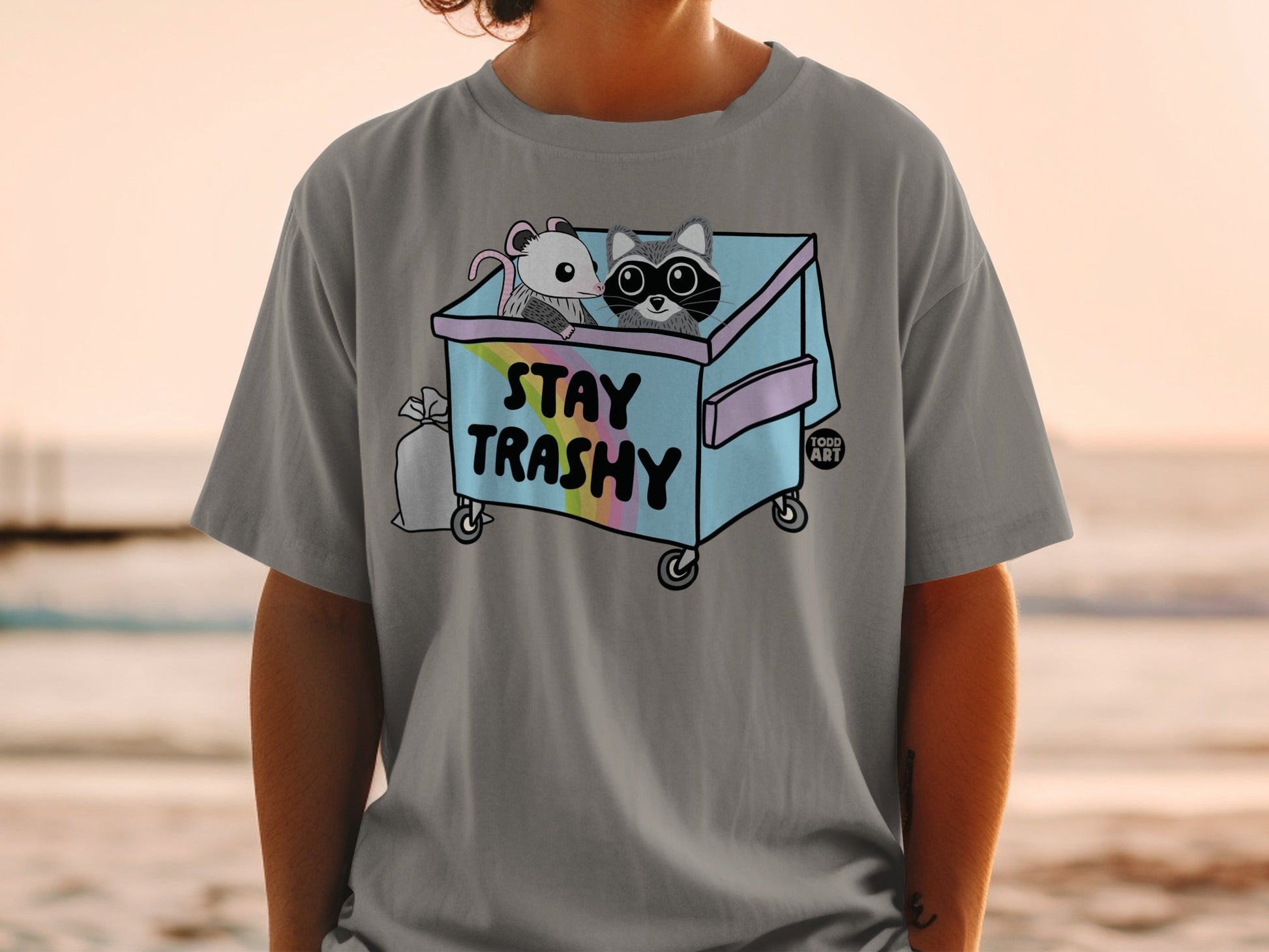 T-shirt with cartoon raccoon and possum in a trash can, text "Stay Trashy".