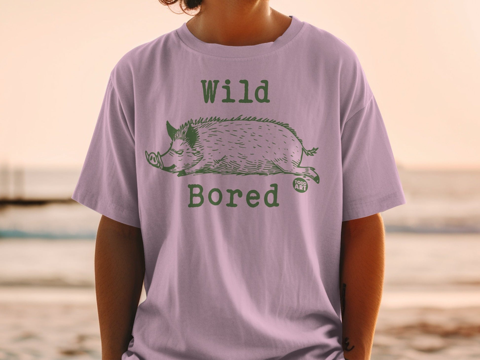 Purple t-shirt with a green illustration of a wild boar and text "Wild Bored".