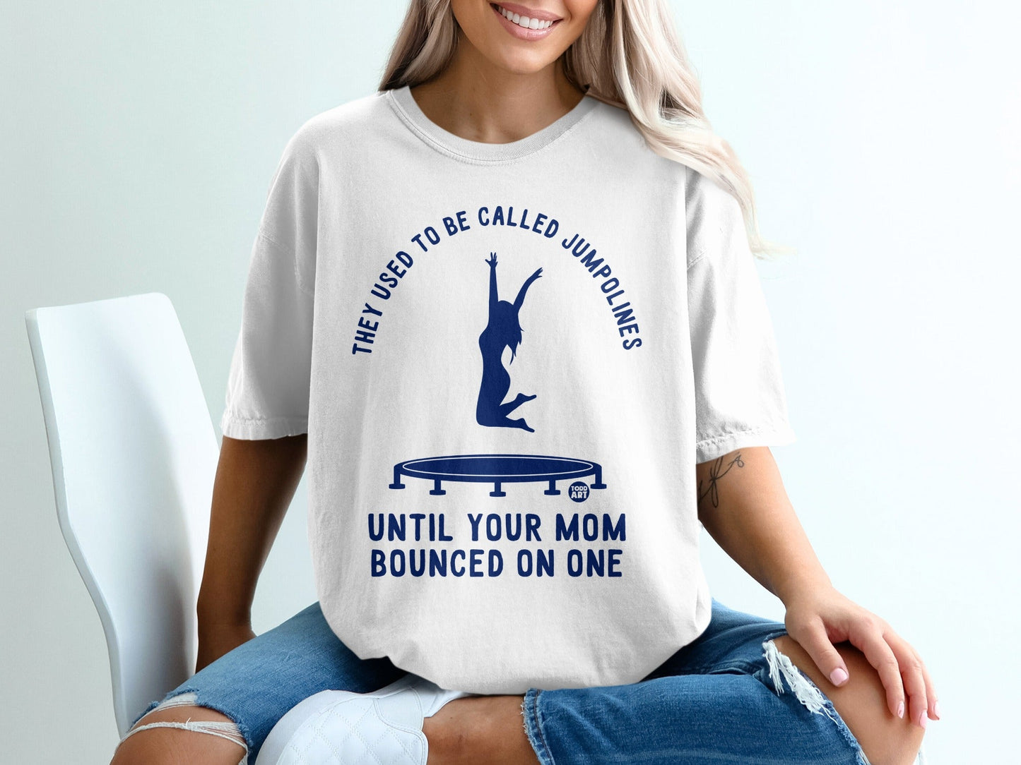 White t-shirt with blue text and trampoline graphic, "They Used To Be Called Jumpolines Until Your Mom Bounced On One."