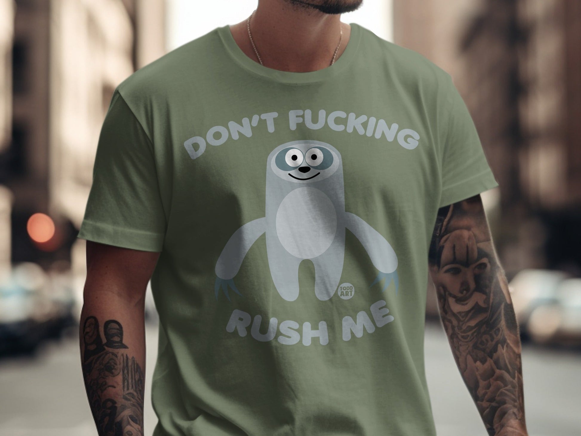 Olive green t-shirt with cartoon sloth graphic and text "DON'T FUCKING RUSH ME".