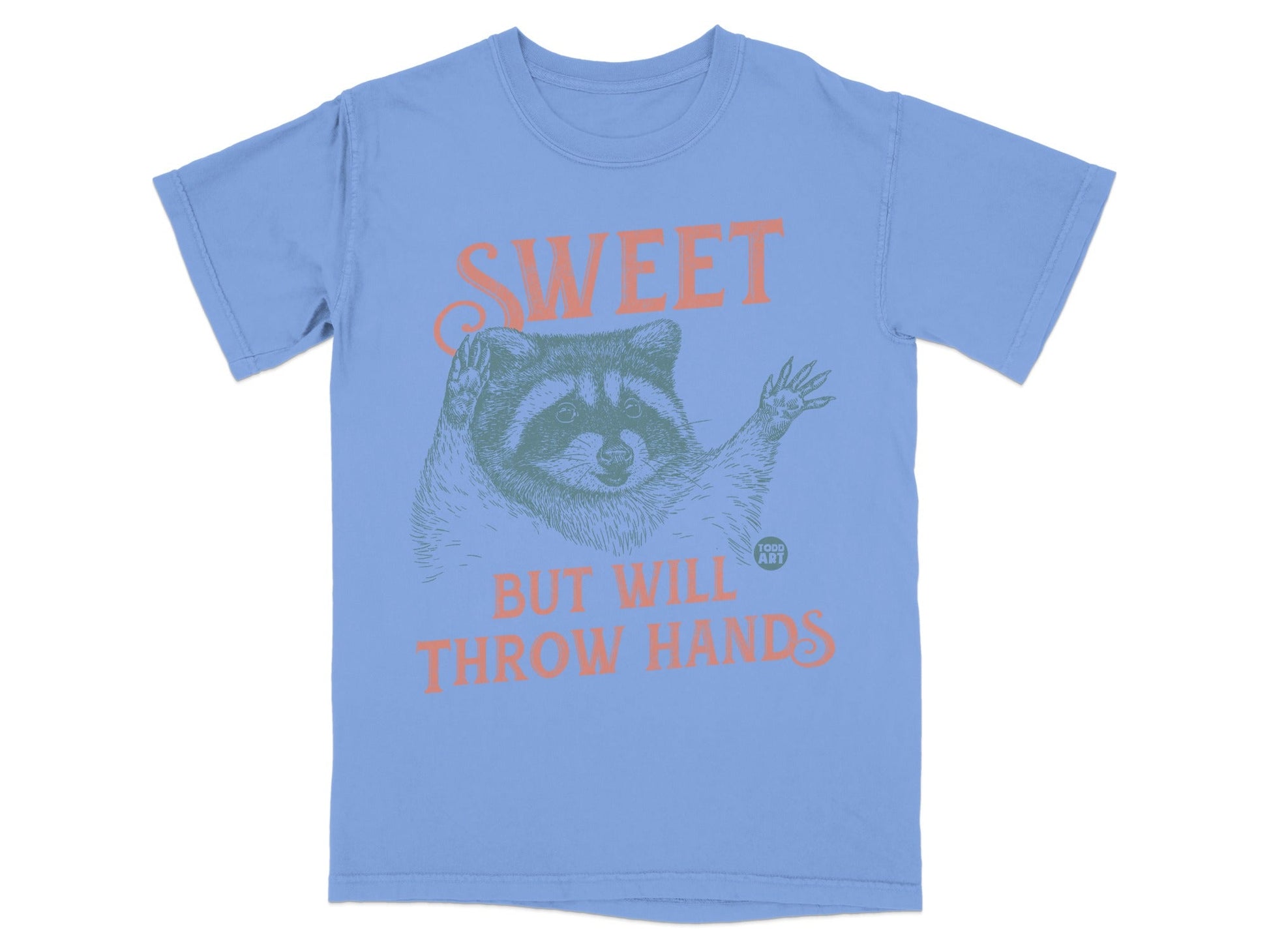 Blue t-shirt with raccoon illustration and text "SWEET BUT WILL THROW HANDS."