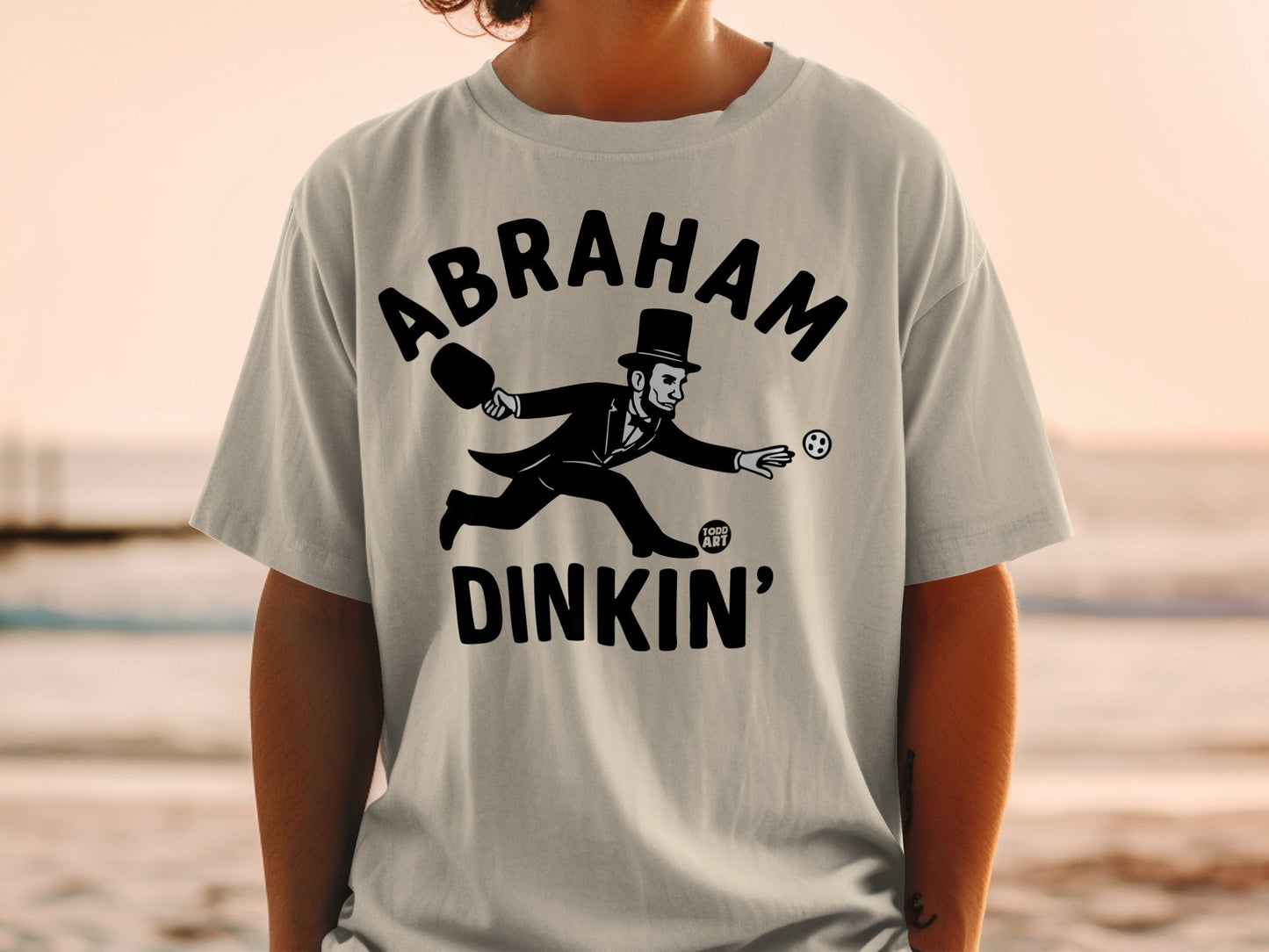 T-shirt with Abraham Lincoln playing pickleball, "Abraham Dinkin'" text.