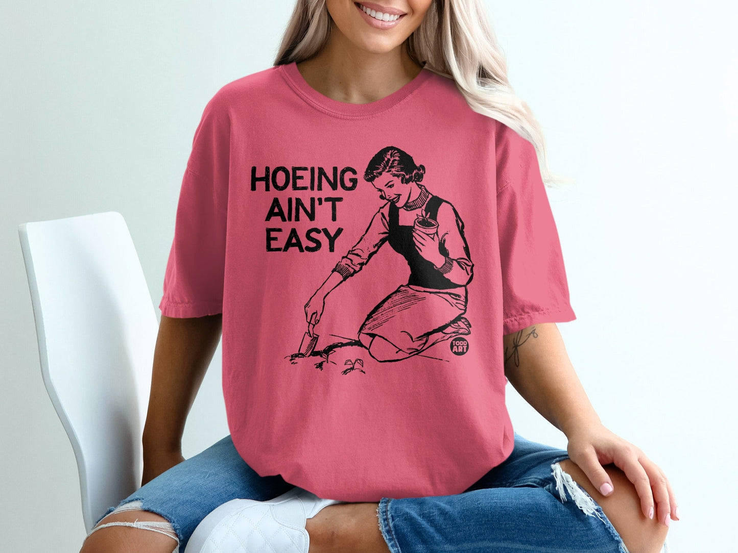 T-shirt with graphic of woman gardening and text "Hoeing ain't easy".