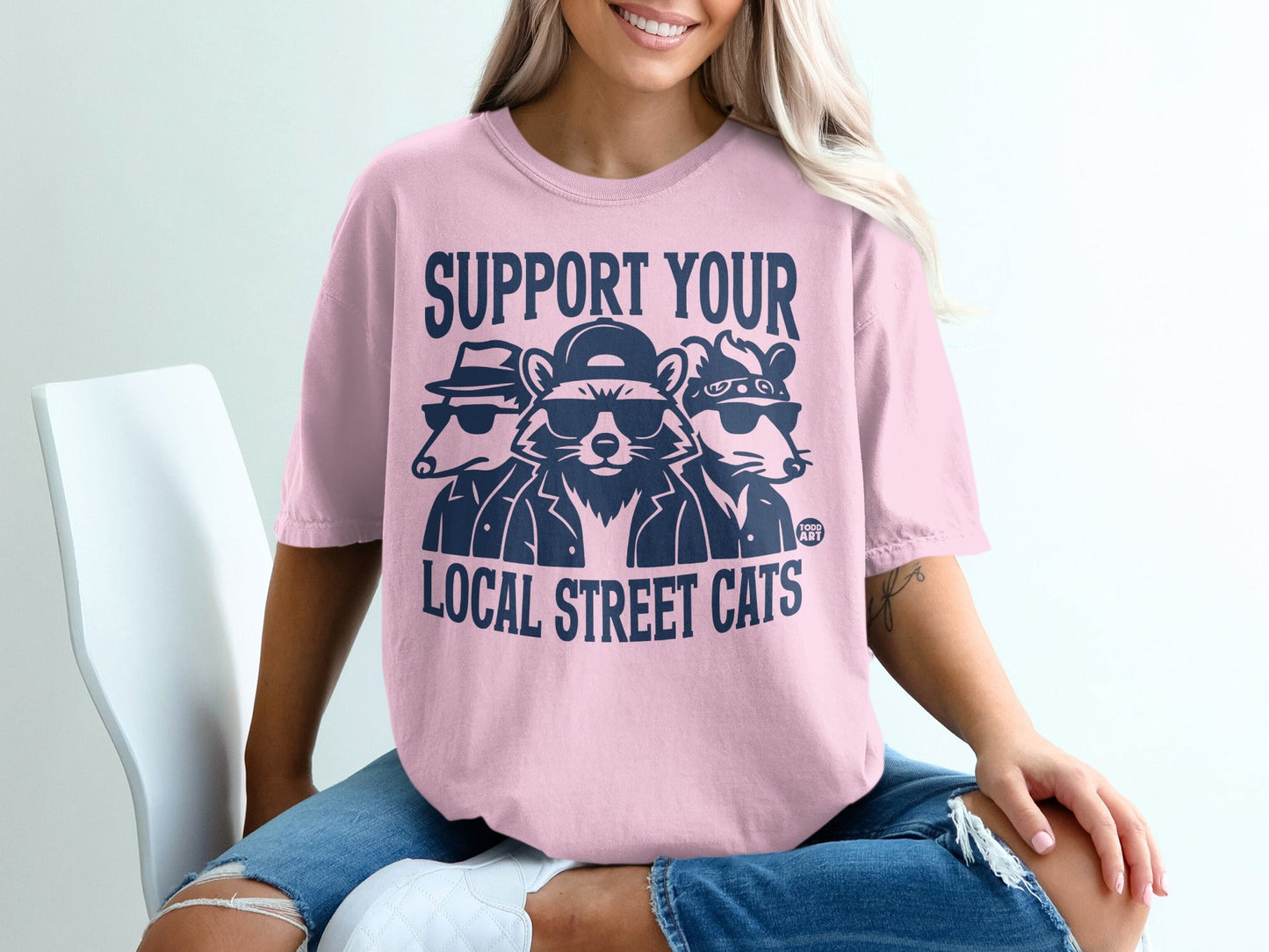 Pink t-shirt with navy blue text and graphic of three raccoons.