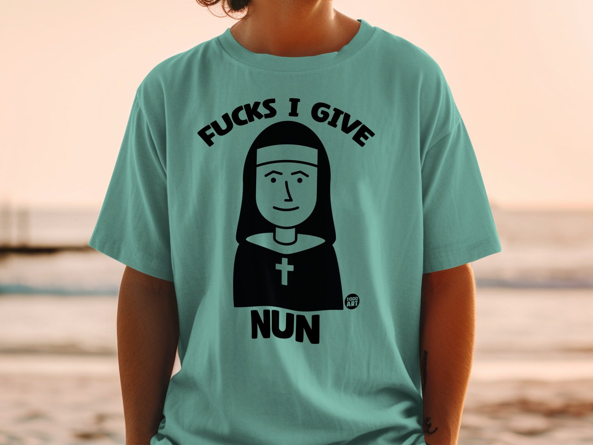 Teal t-shirt with "Fucks I Give Nun" graphic and cross emblem.
