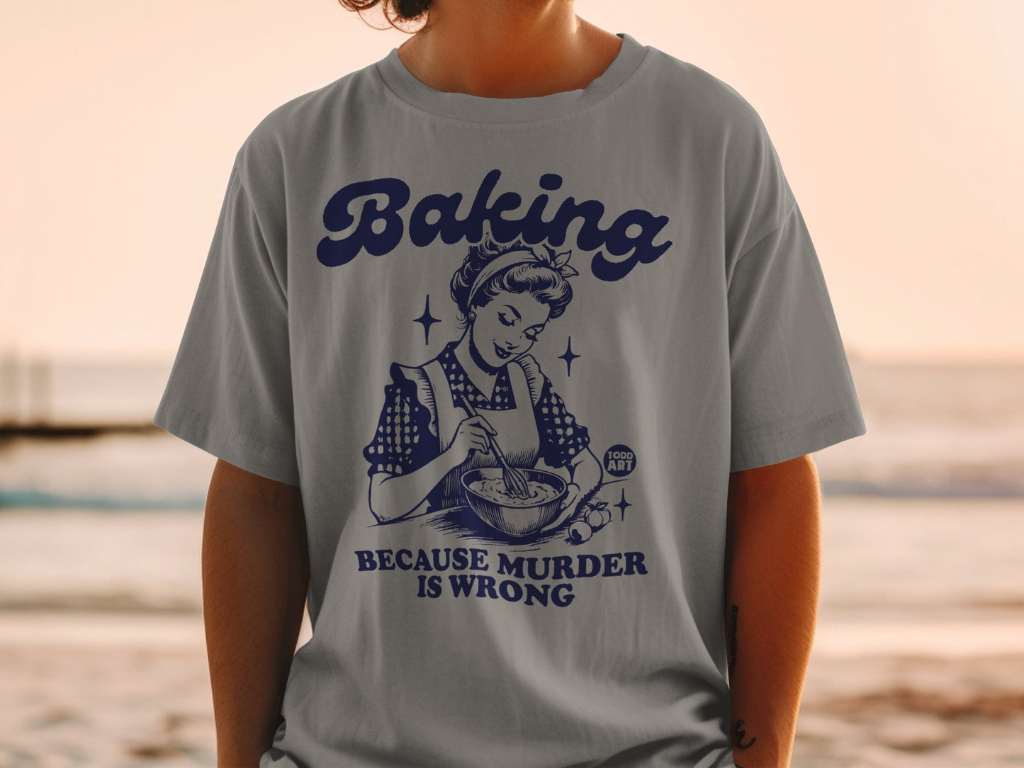 Grey t-shirt with retro graphic of woman baking and text "Baking because murder is wrong".