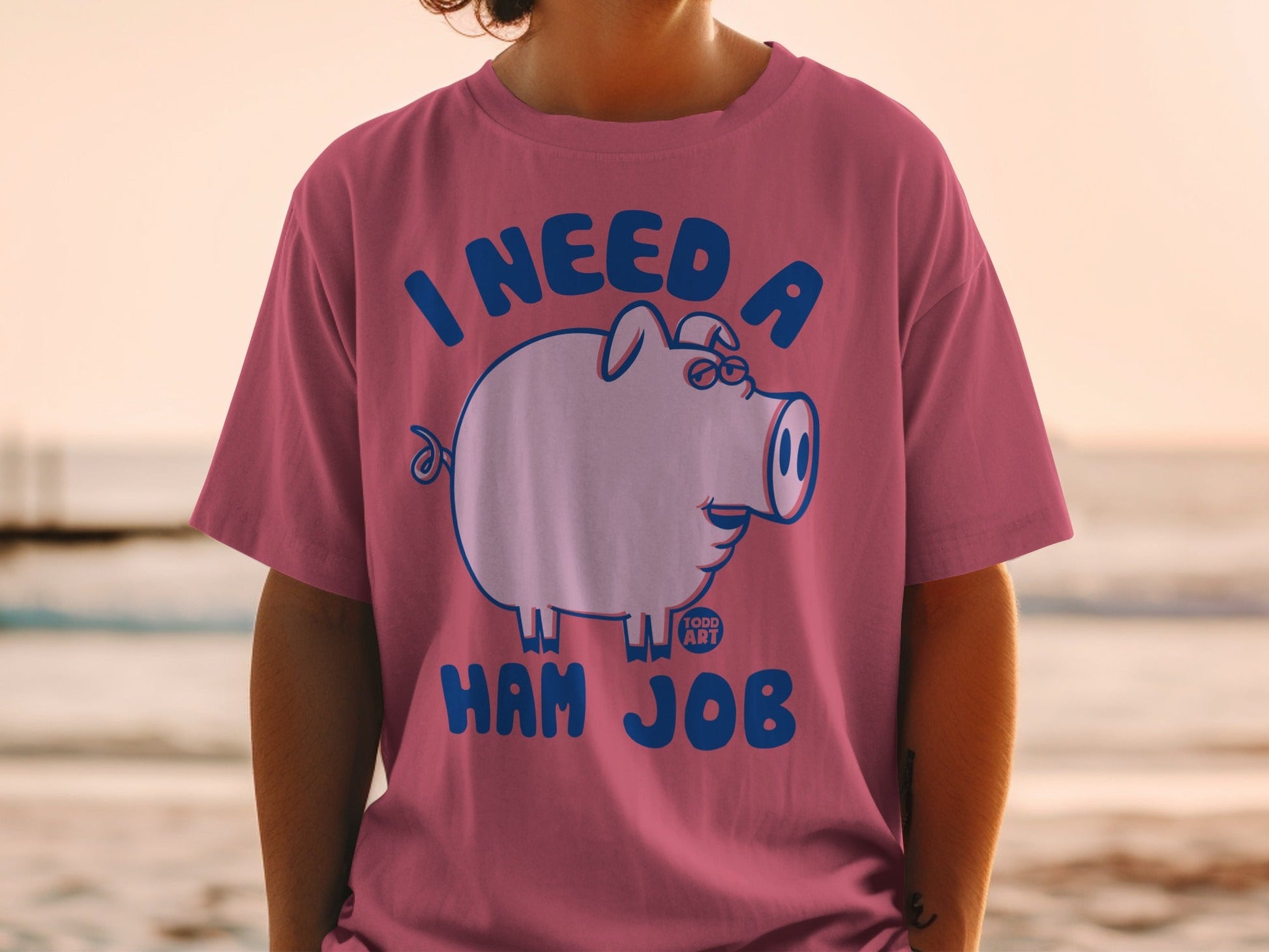 Pink t-shirt with a cartoon pig wearing glasses and text that reads "I NEED A HAM JOB".