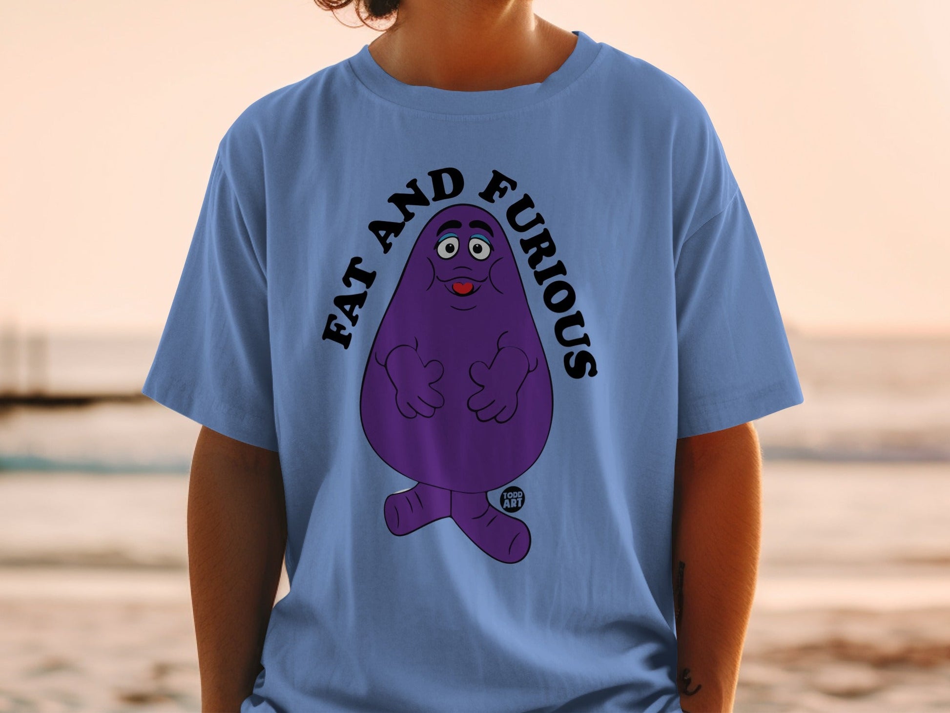 Purple Grimace character wearing a blue t-shirt that says "FAT AND FURIOUS".