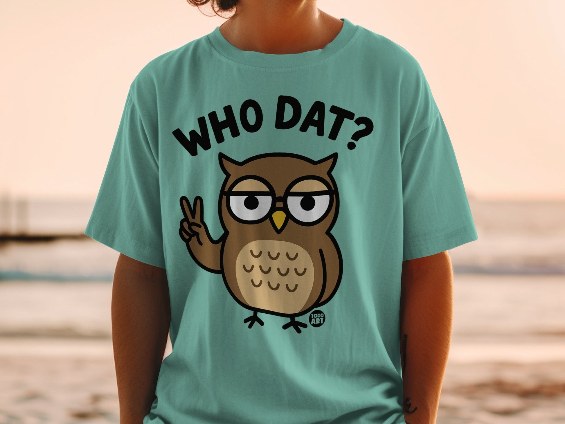 Teal t-shirt with cartoon owl saying "WHO DAT?" and holding up a peace sign.