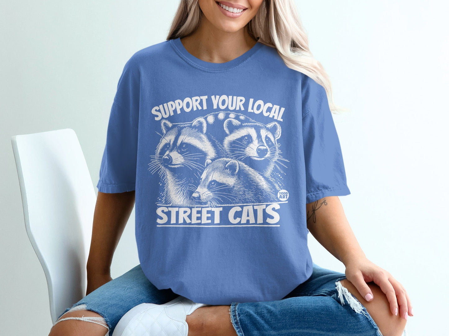 Graphic t-shirt with three raccoons and text "SUPPORT YOUR LOCAL STREET CATS".