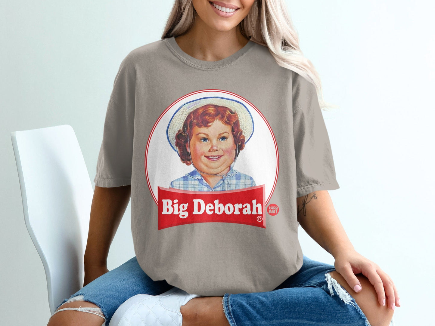 Woman wearing a taupe t-shirt with "Big Deborah" logo and vintage child illustration.