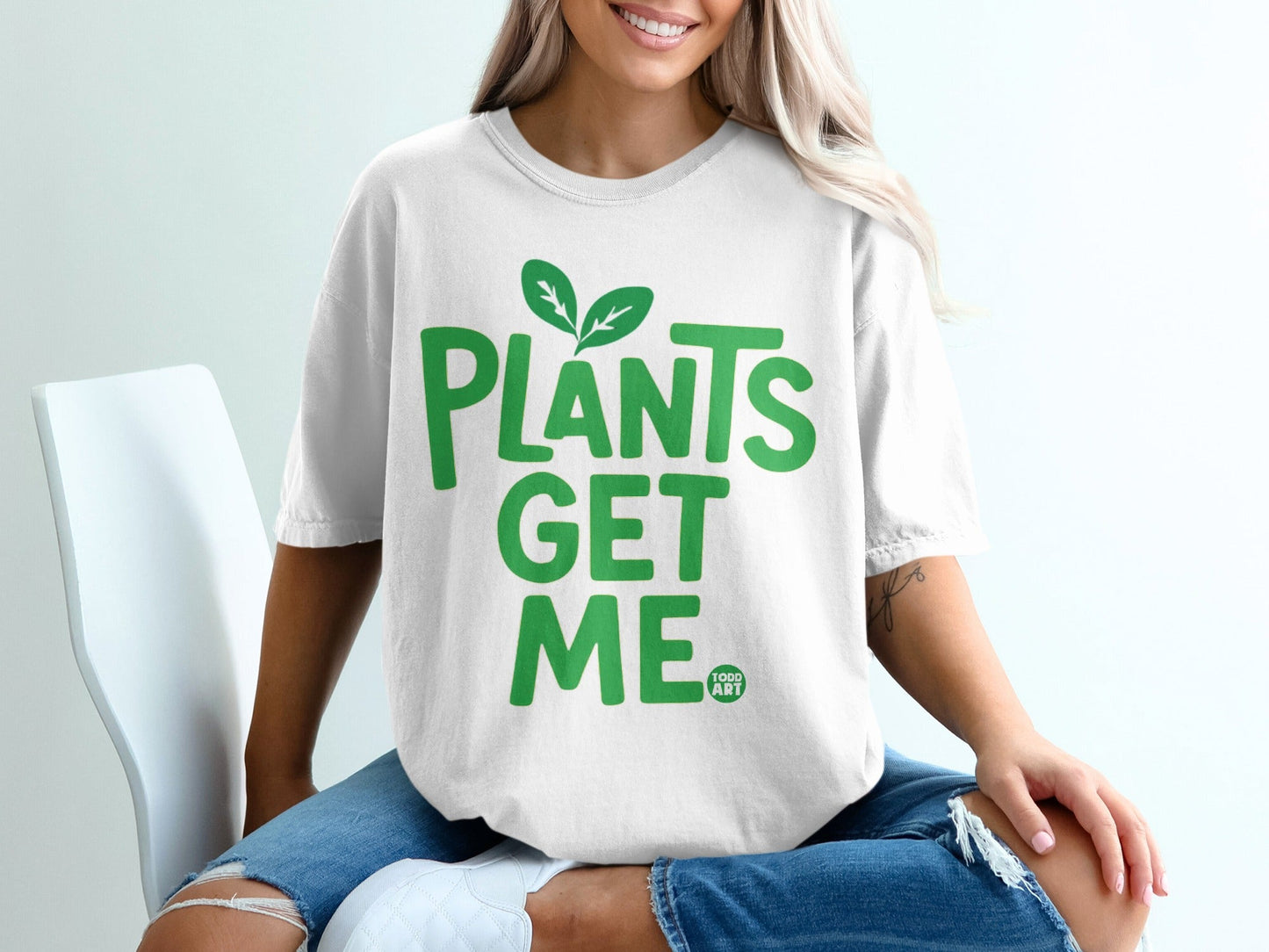 White t-shirt with green text "PLANTS GET ME" and two leaves.