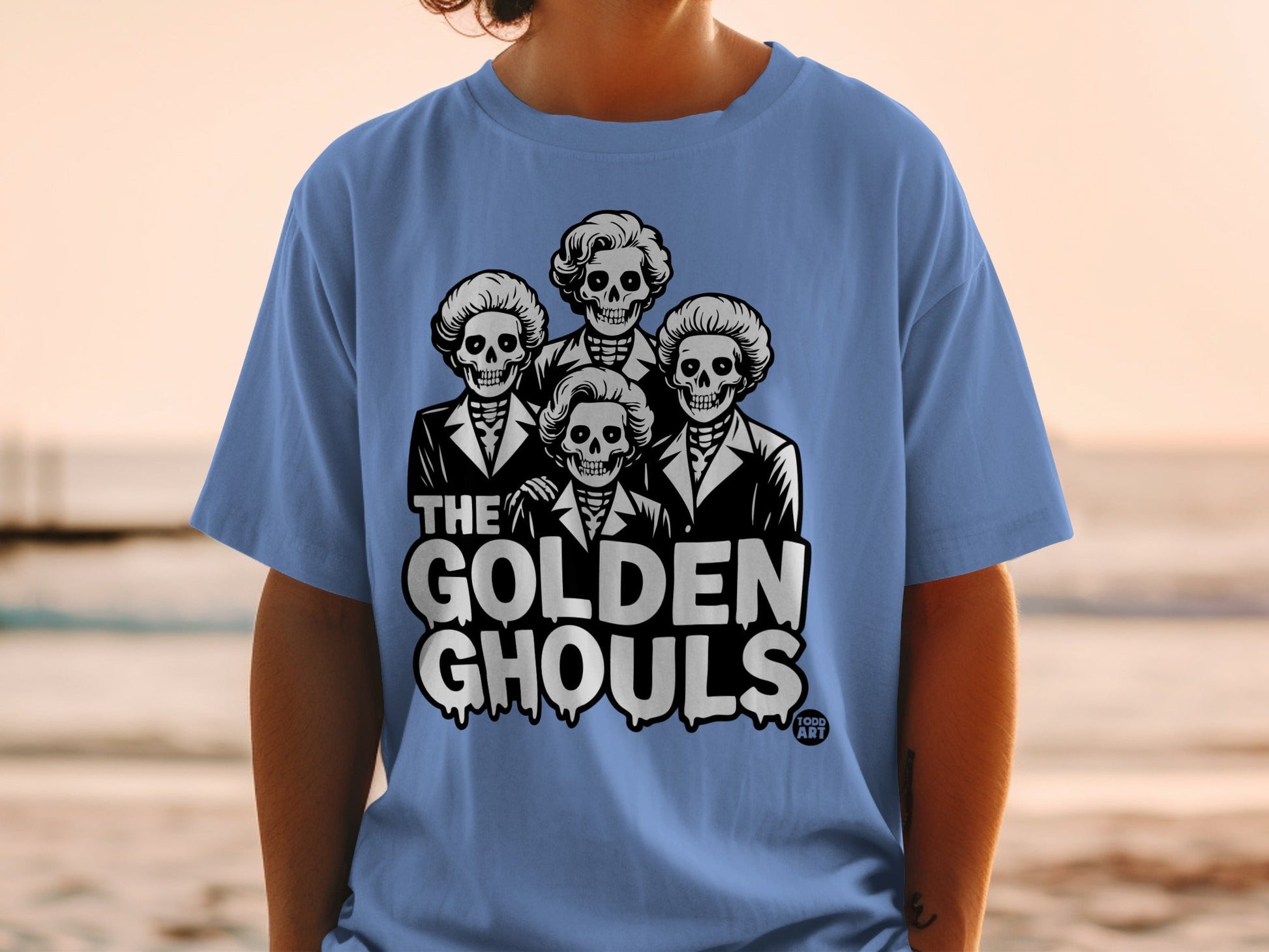 Light blue t-shirt with "THE GOLDEN GHOULS" and four skeleton heads graphic.