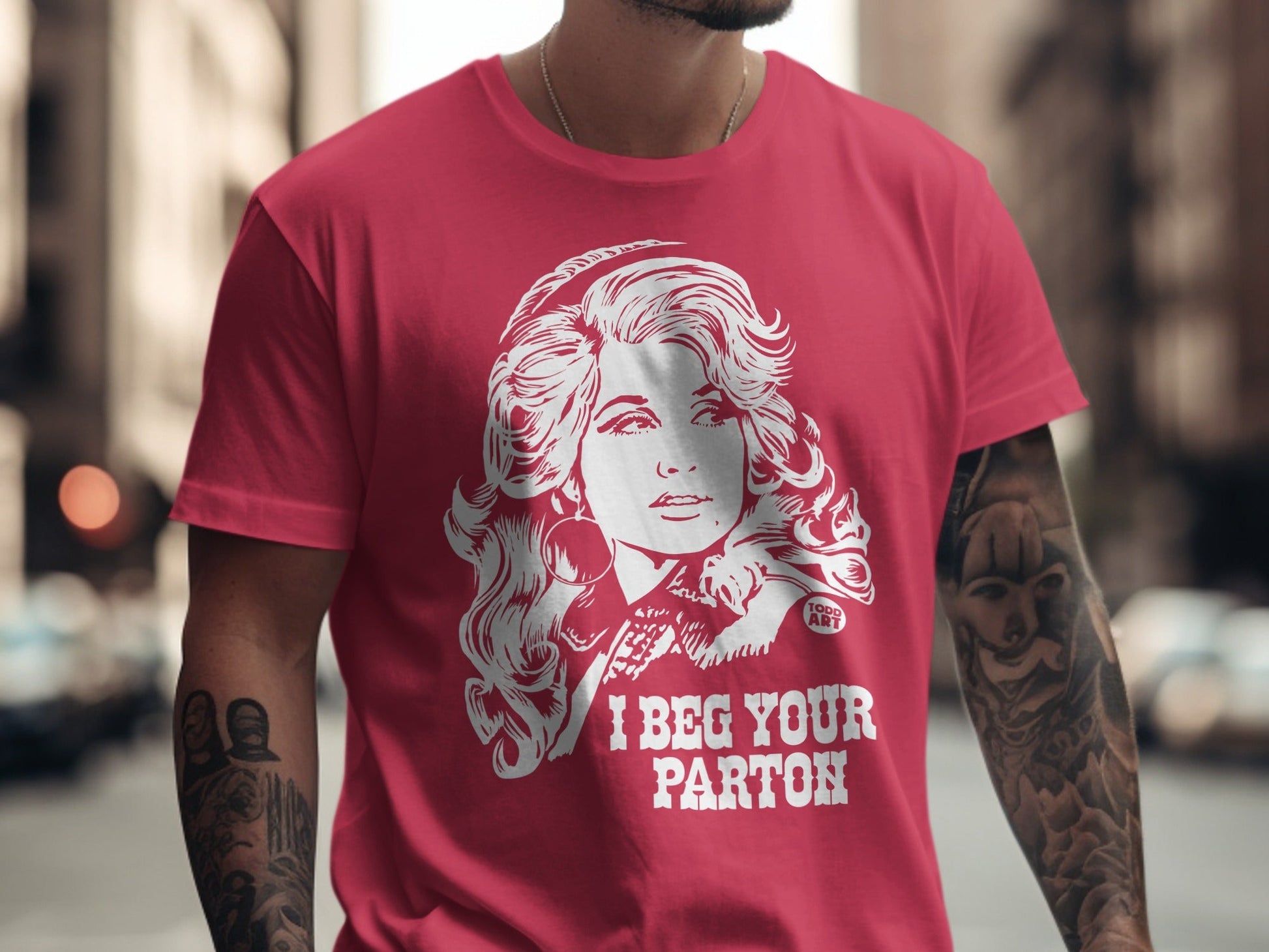 Red t-shirt with white graphic of Dolly Parton and "I BEG YOUR PARTON" text.