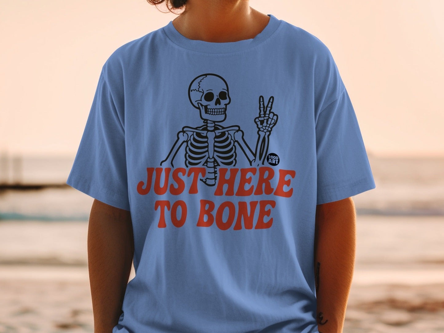 Blue t-shirt with skeleton and text "JUST HERE TO BONE"