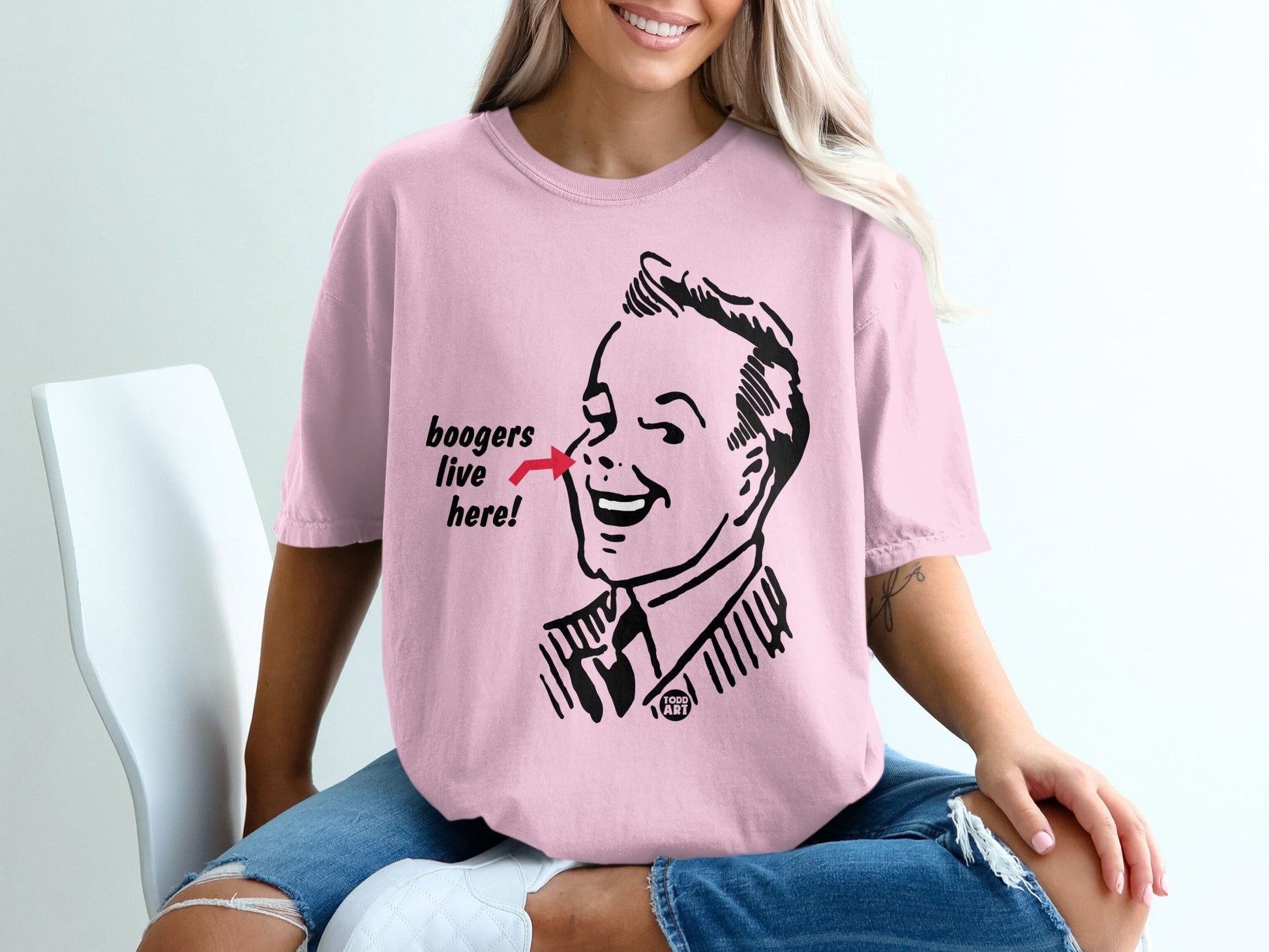 Pink t-shirt with cartoon man pointing to nose that says "boogers live here."