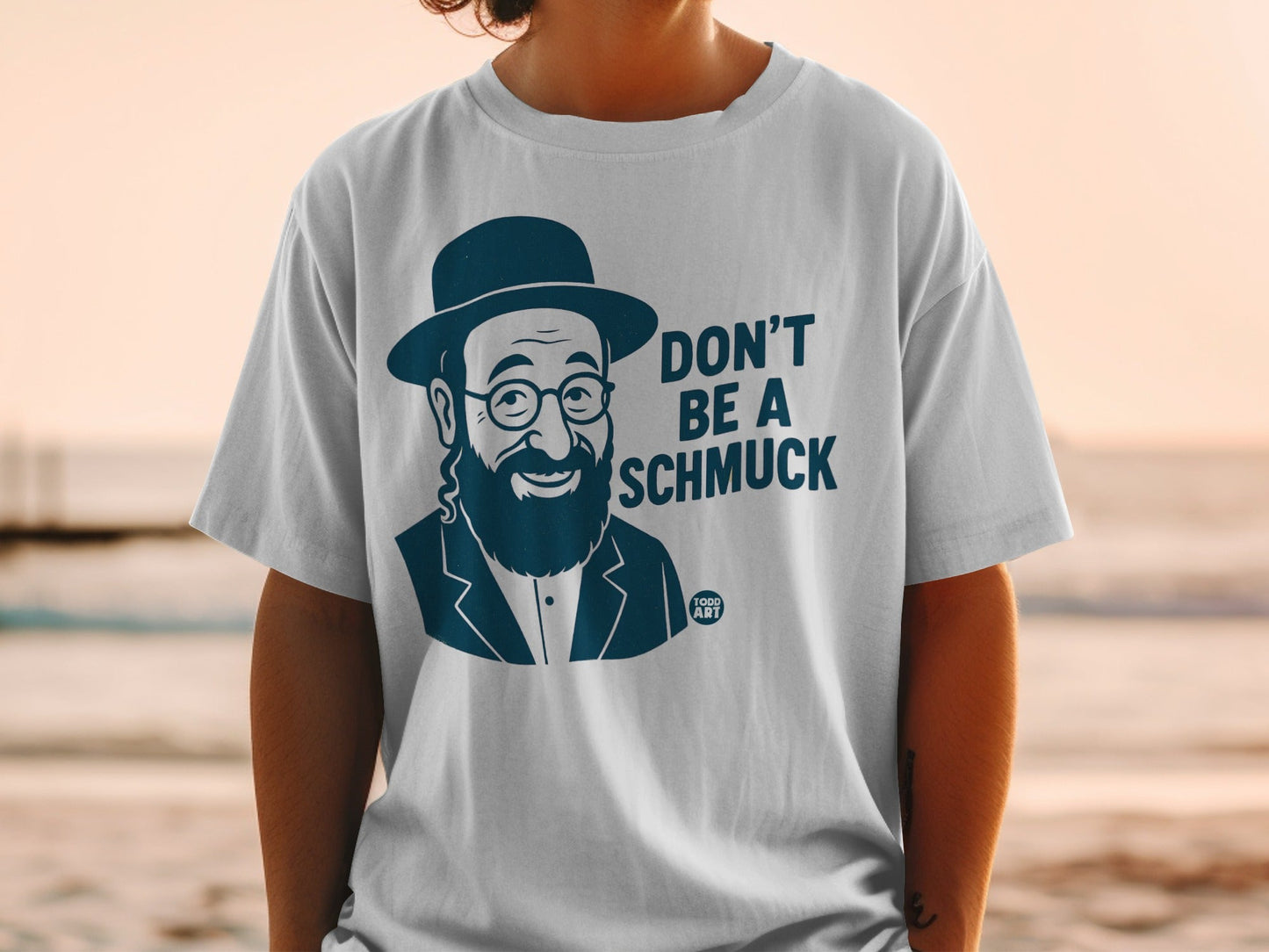White t-shirt with a graphic of a smiling man in a hat and the text "DON'T BE A SCHMUCK".