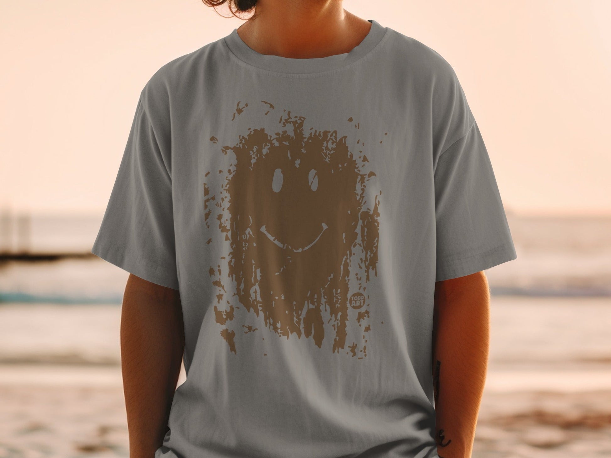 Grey t-shirt with a distressed brown smiley face graphic on a person.