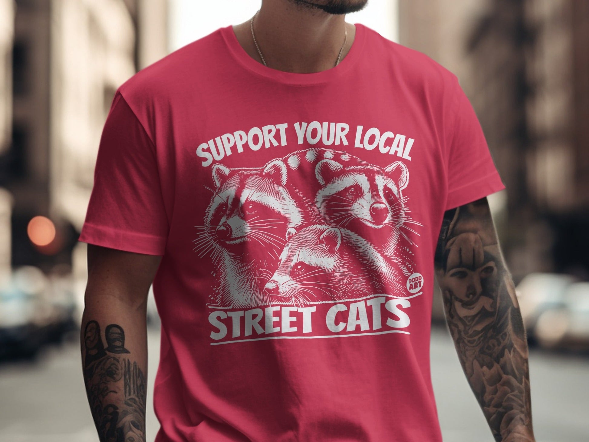 Red t-shirt with graphic of three raccoons and text "SUPPORT YOUR LOCAL STREET CATS".