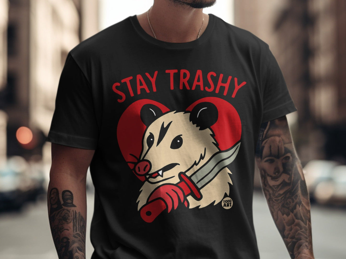 Black t-shirt with "Stay Trashy" text and cartoon possum holding a knife.