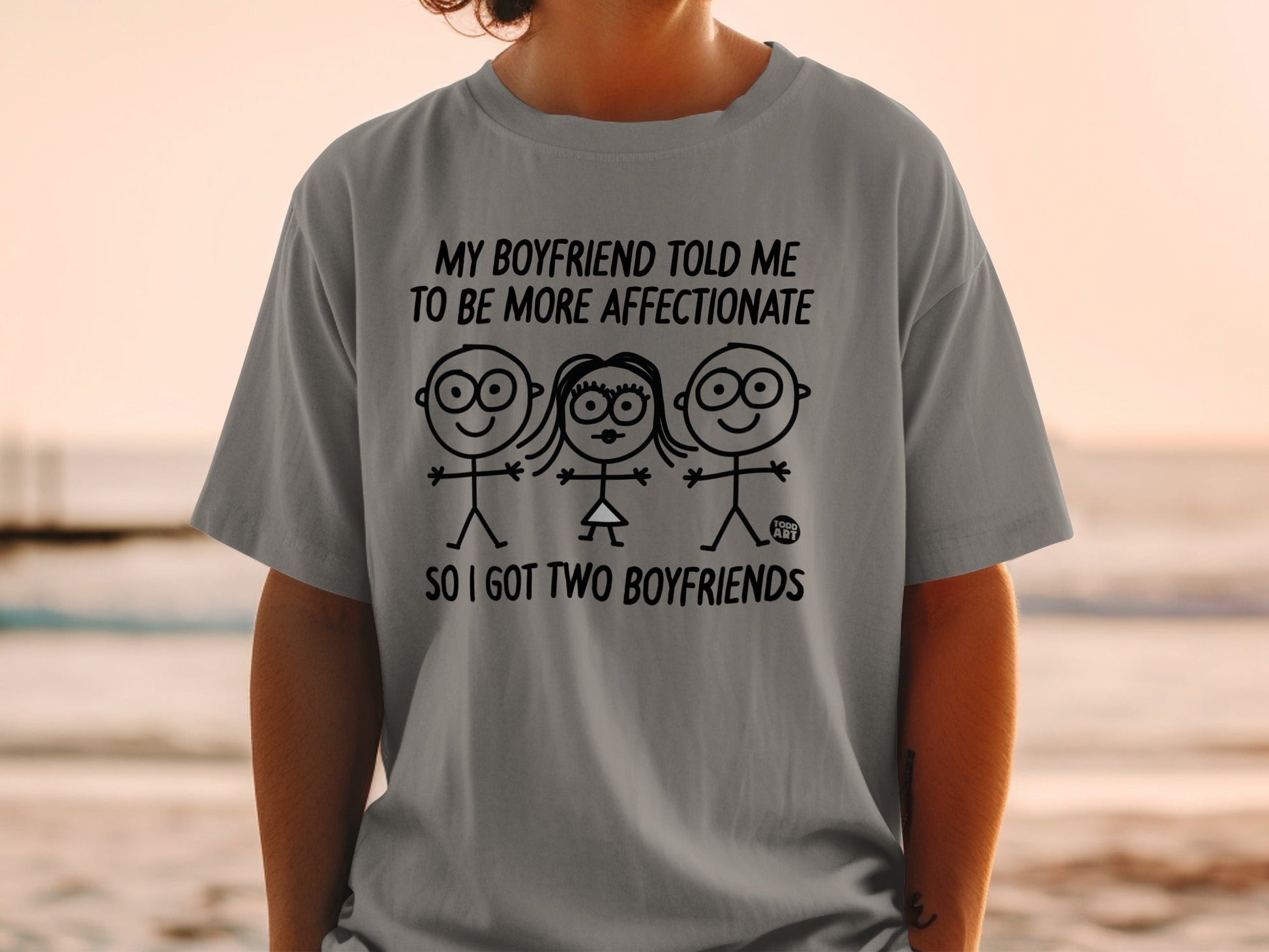 Grey t-shirt with cartoon figures and text: "My boyfriend told me to be more affectionate so I got two boyfriends."