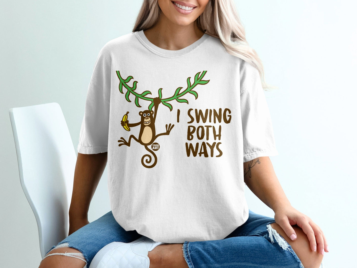 White t-shirt with a cartoon monkey holding a banana and text "I SWING BOTH WAYS".