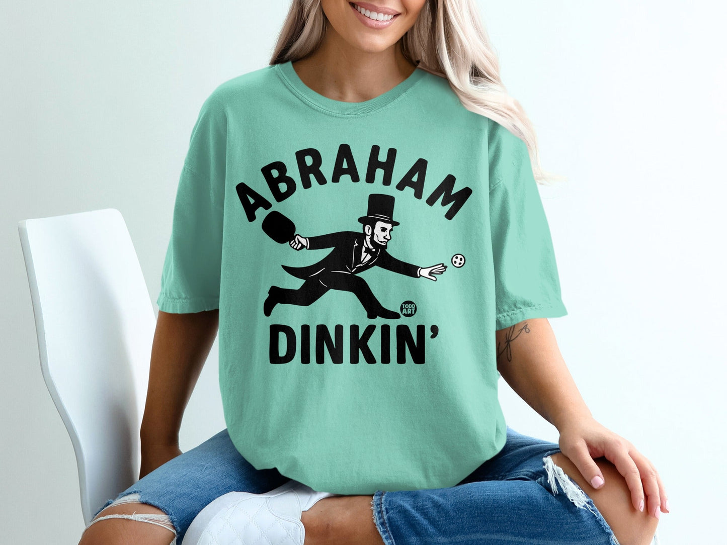 Abraham Lincoln playing croquet on a mint green t-shirt.
