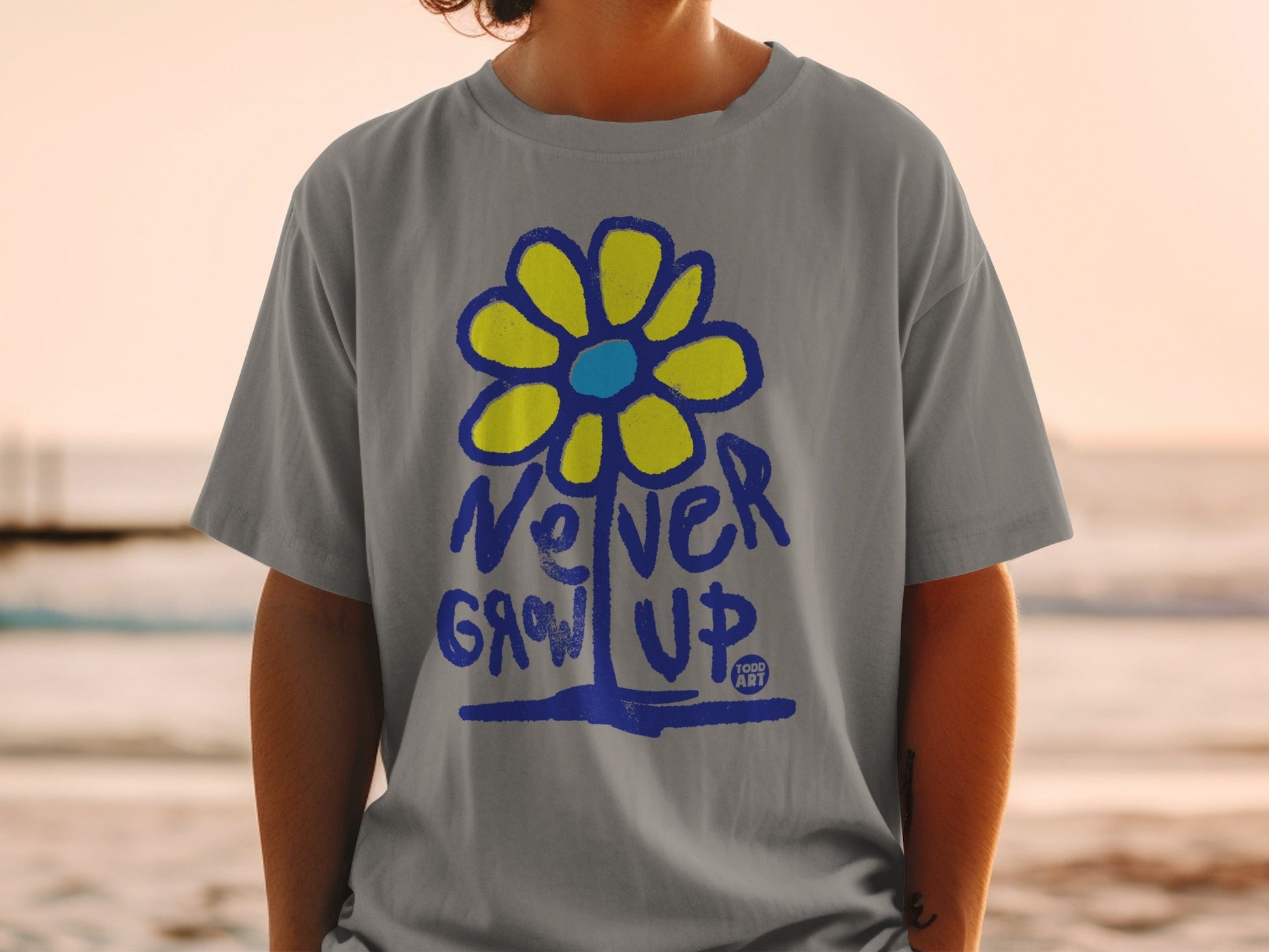 Gray t-shirt with blue and yellow flower graphic and "Never Grow Up" text.