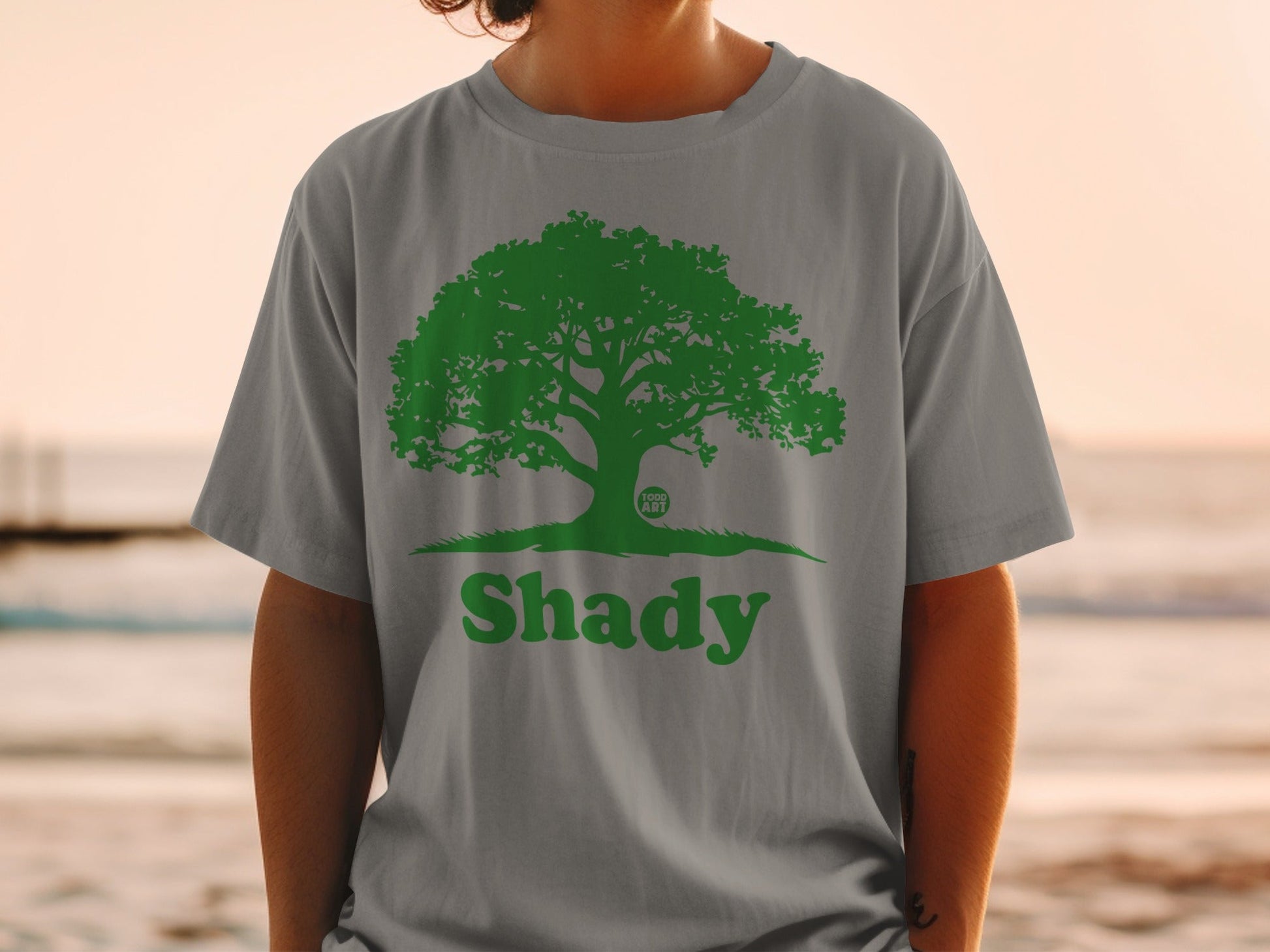 Green tree logo with "Shady" text on a grey t-shirt.