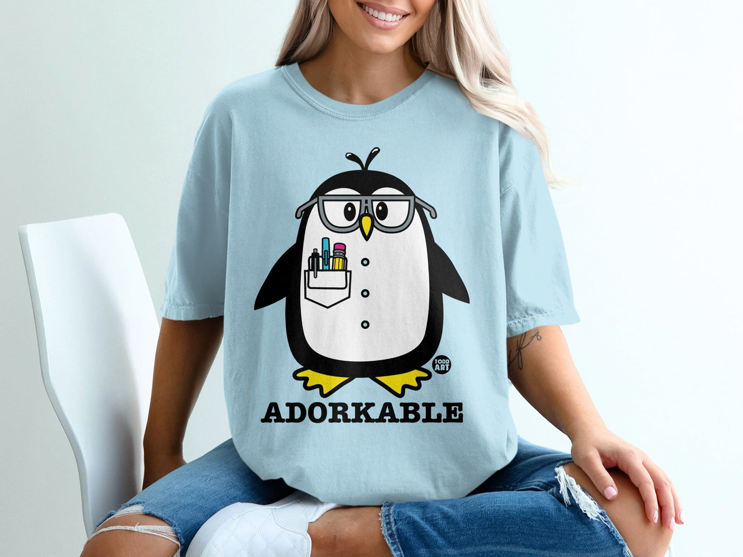 Light blue t-shirt with a cartoon penguin wearing glasses and holding pens.