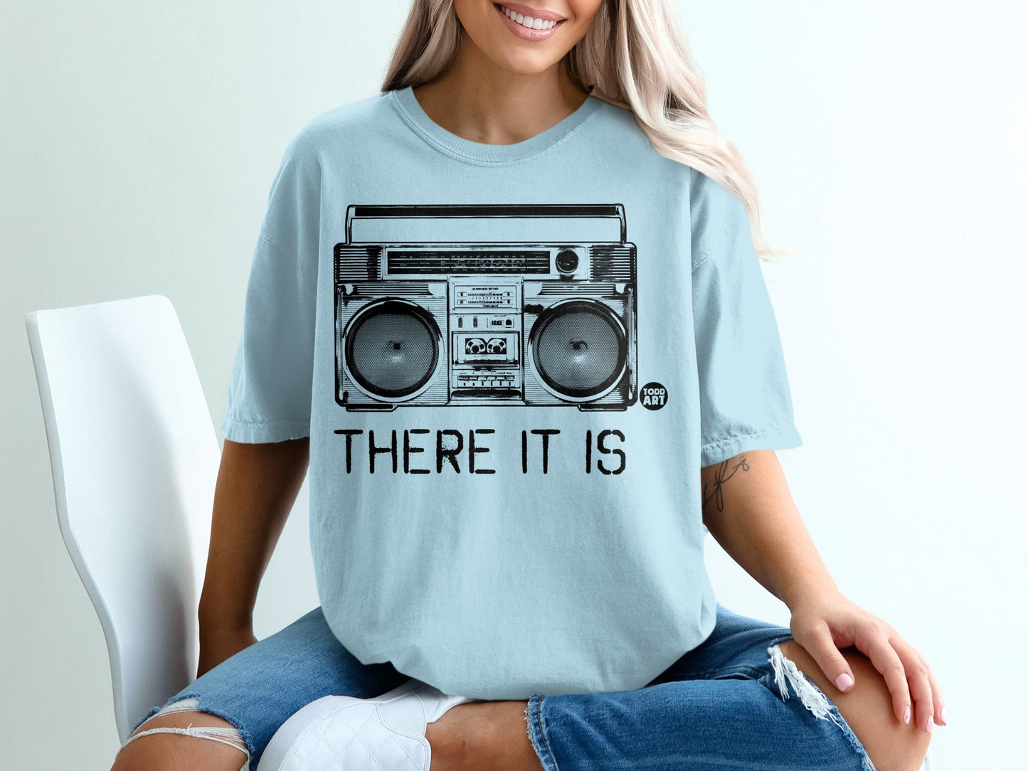 Light blue t-shirt with black graphic of a boombox and text "THERE IT IS" and "1000 ART".