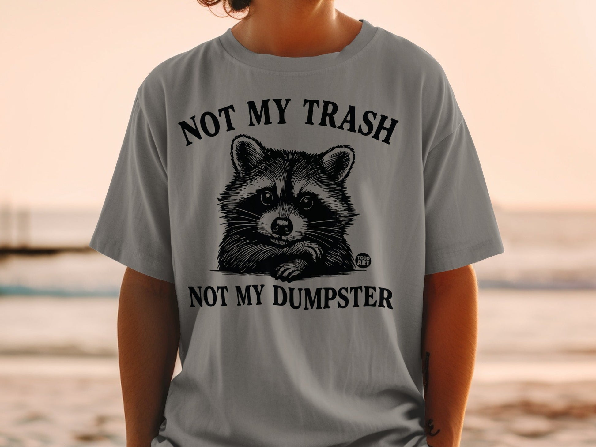Graphic t-shirt with a raccoon and text "NOT MY TRASH NOT MY DUMPSTER".