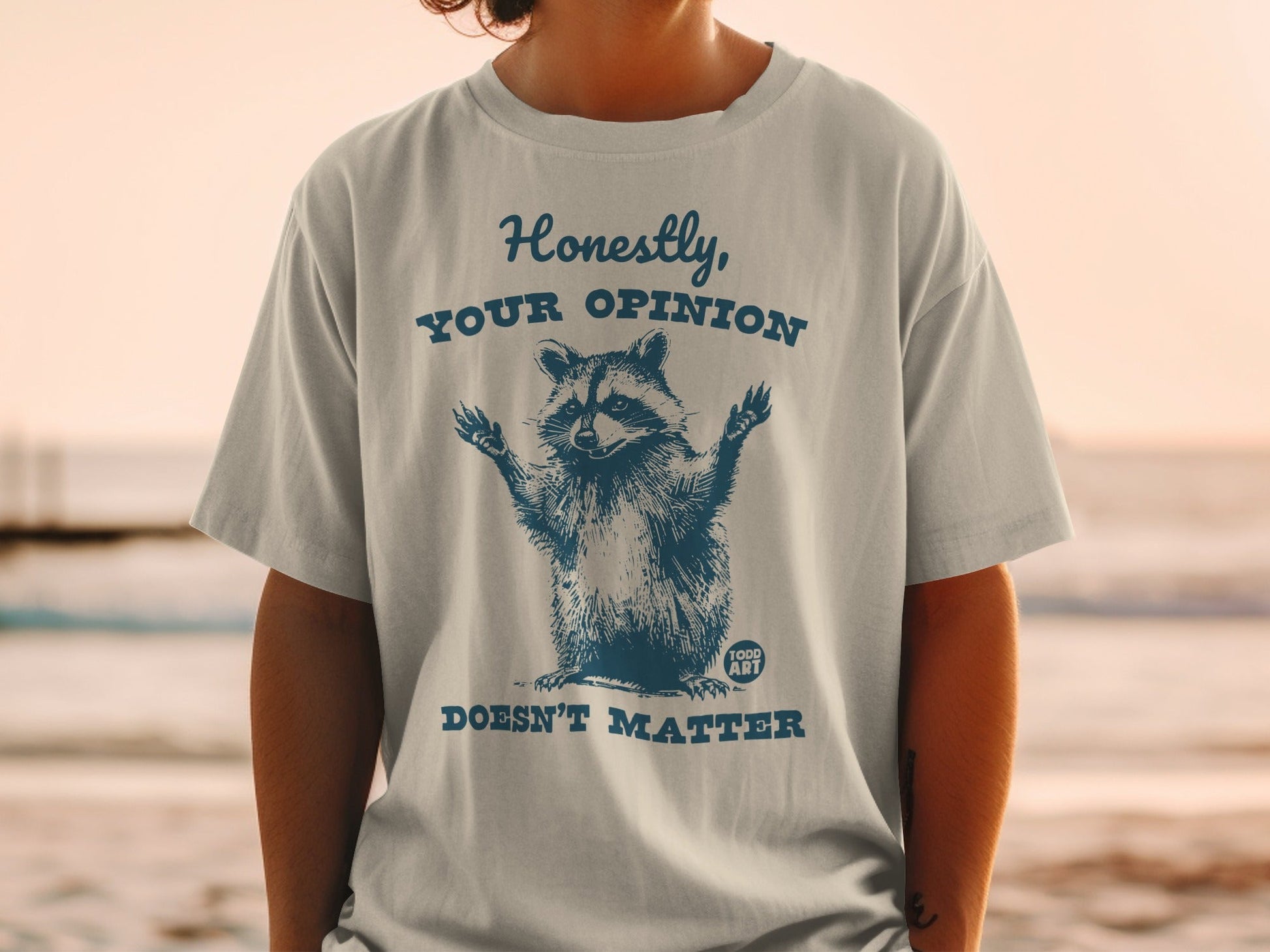White t-shirt with blue raccoon graphic and text "Honestly, your opinion doesn't matter."