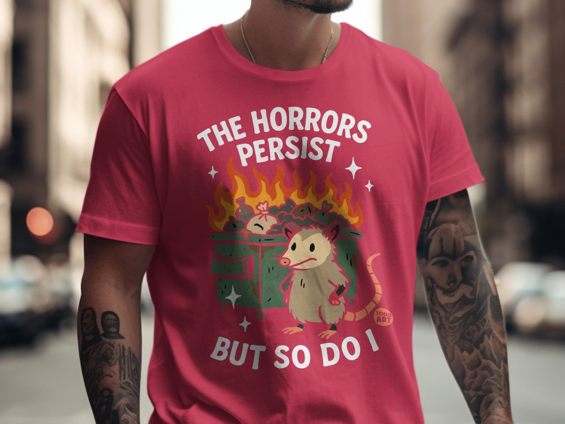 T-shirt with possum and burning dumpster graphic, text "The Horrors Persist But So Do I".