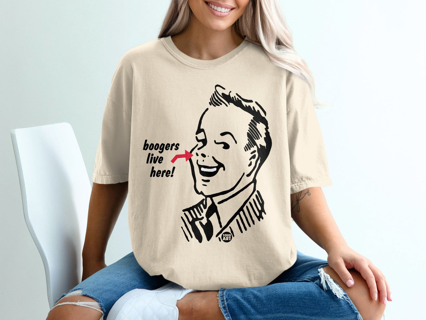 Cream t-shirt with retro illustration of a man pointing at his nose with text "boogers live here!".